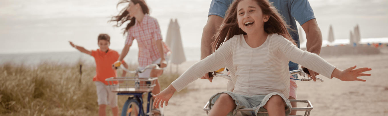 A smiling girl rides a bike near the beach