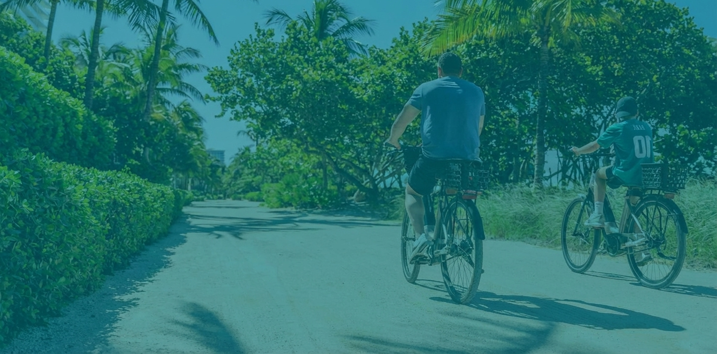 Two males on bikes, riding along beach path.