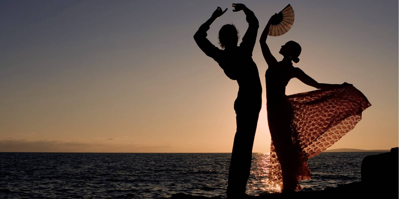 Flamenco guitarist and dancer perform by the water during sunset.