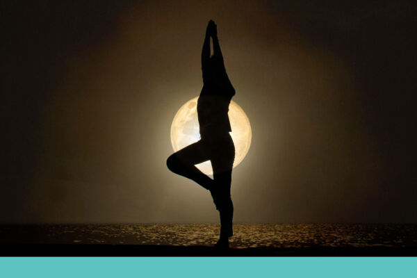 A woman in a yoga pose on the beach with the moon in the background.