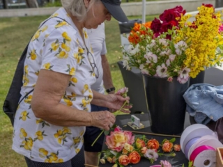 COMPRESSEDFleursDeVilles2024 PARK 03-02-24_8 (1) A woman leaning forward looking at the flowers on the table, choosing which flower to add to her bouquet.