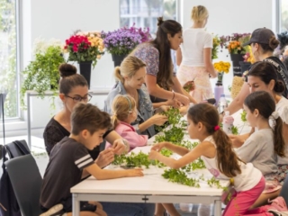 COMPRESSEDFleursDeVilles2024 PARK 03-03-24 _12 (1) A group of children and adults sitting at a table, starting the process of creating their flower crowns.
