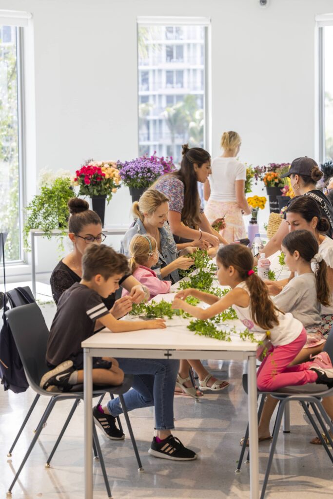 A group of children and adults sitting at a table, starting the process of creating their flower crowns.