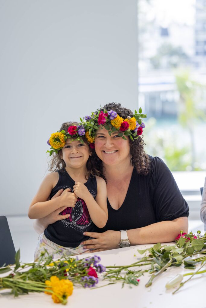 A woman and her daughter smiling for the camera, wearing the flower crowns they just made.