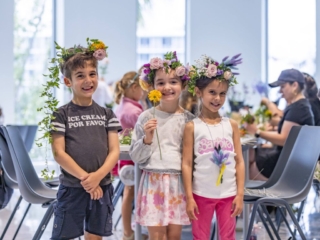 COMPRESSEDFleursDeVilles2024 PARK 03-03-24 _57 (1) Three children smiling for the camera with the flower crowns they made sitting on top of their heads.