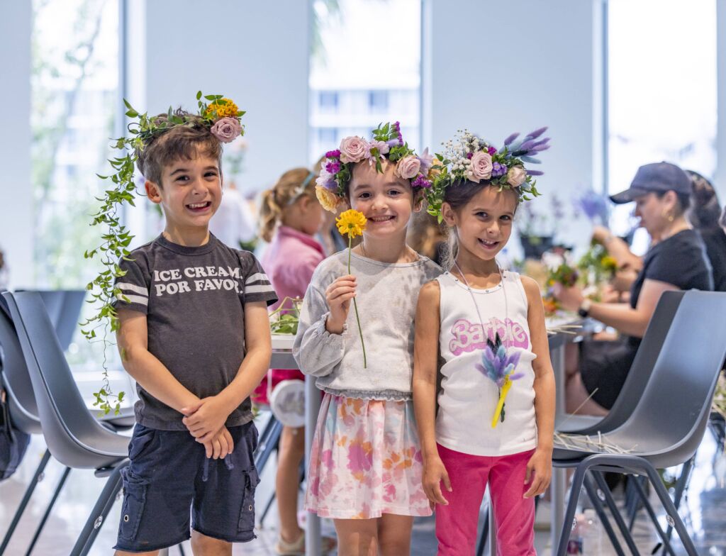 Three children smiling for the camera with the flower crowns they made sitting on top of their heads.