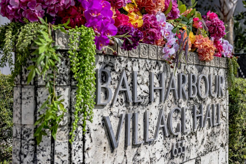 The Bal Harbour Village Hall sign with flowers overflowing the top of it in a multitude of colors and types.