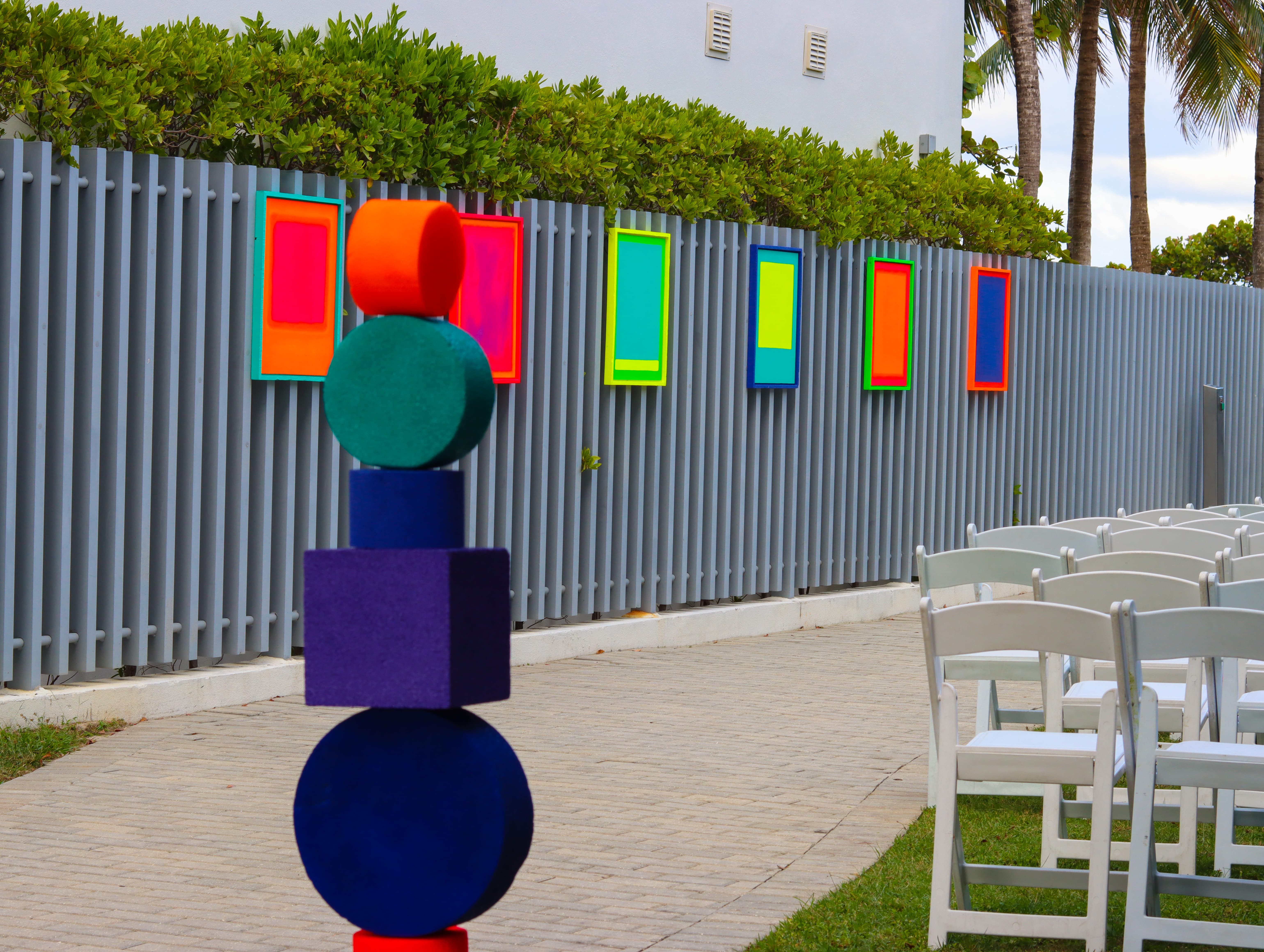 Focused on one of Artist Andreina Ron Pedrique&#039;s colorful sculptures. There is a row of her colorful work in the near distance and white chairs peaking out on the right side.