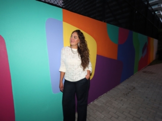 DIC2Compressed Artist Andreina Ron Pedrique staring at her wall art besides her in the Dreaming in color exhibit.