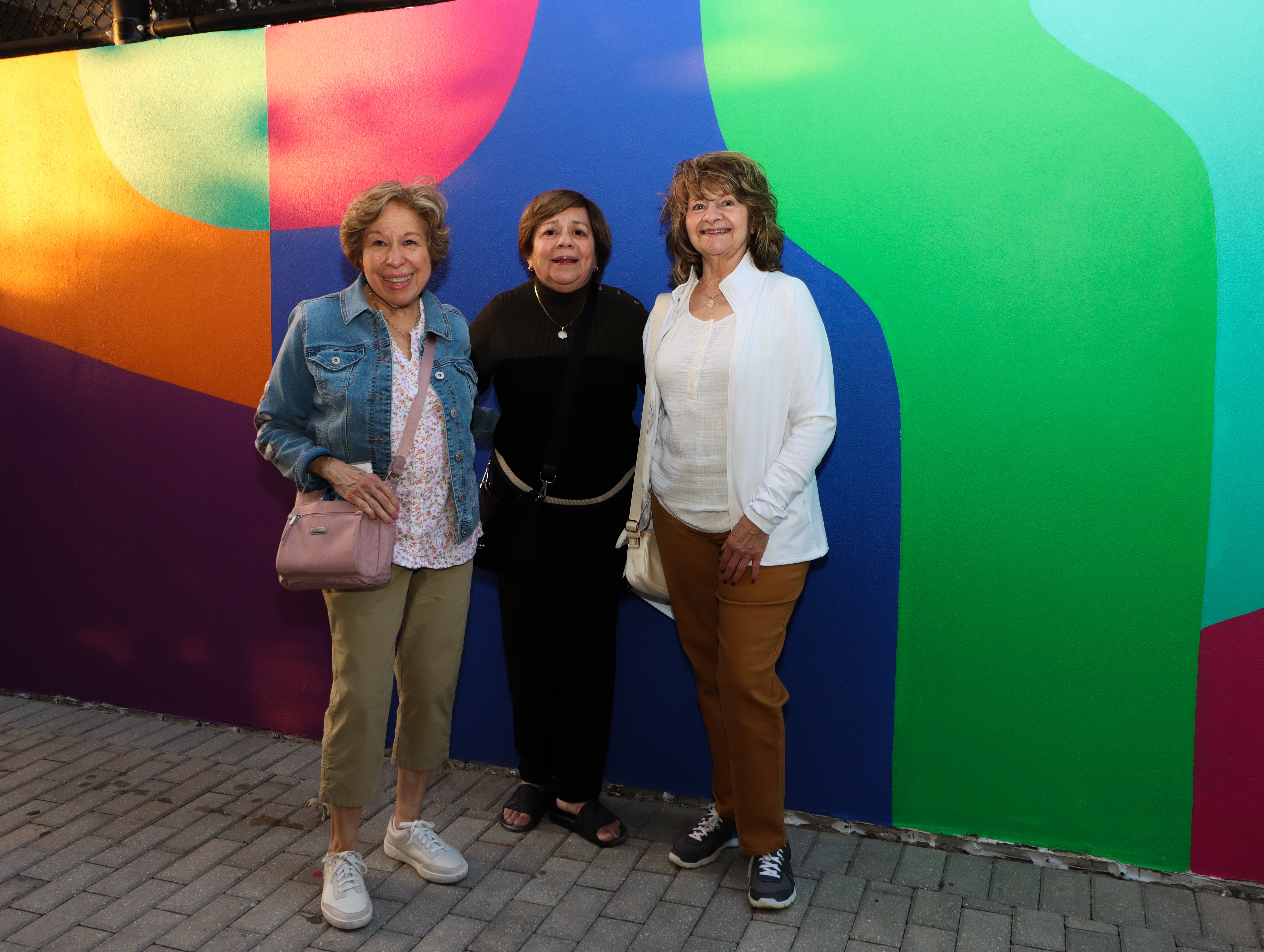 Three women posing for the camera in front of wall art at the Dreaming in Color Exhibit.