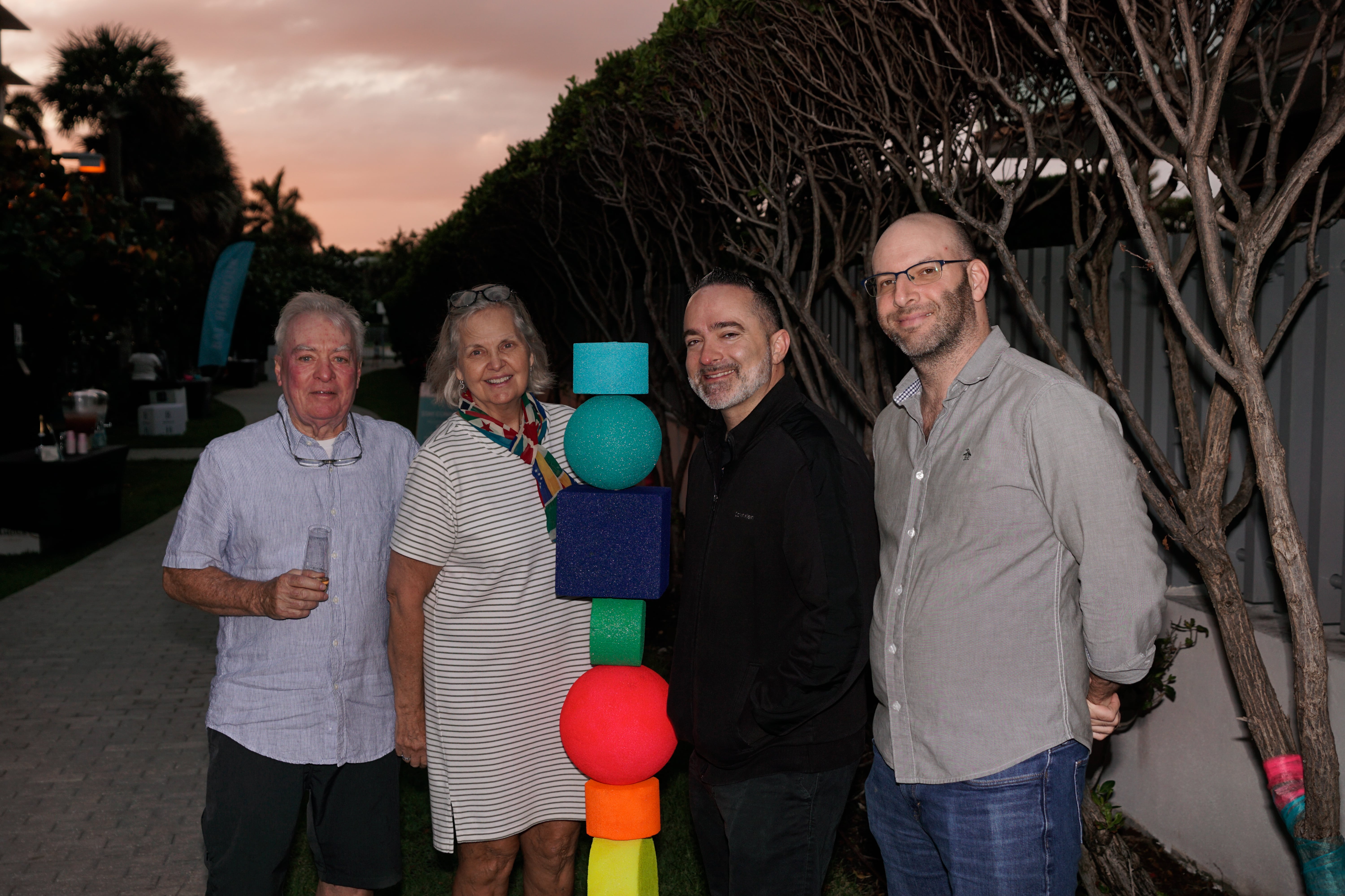 A group of residents smiling next to one of the colorful sculptures at the Dreaming In Color Exhibit. The wishing trees are to their right behind them.