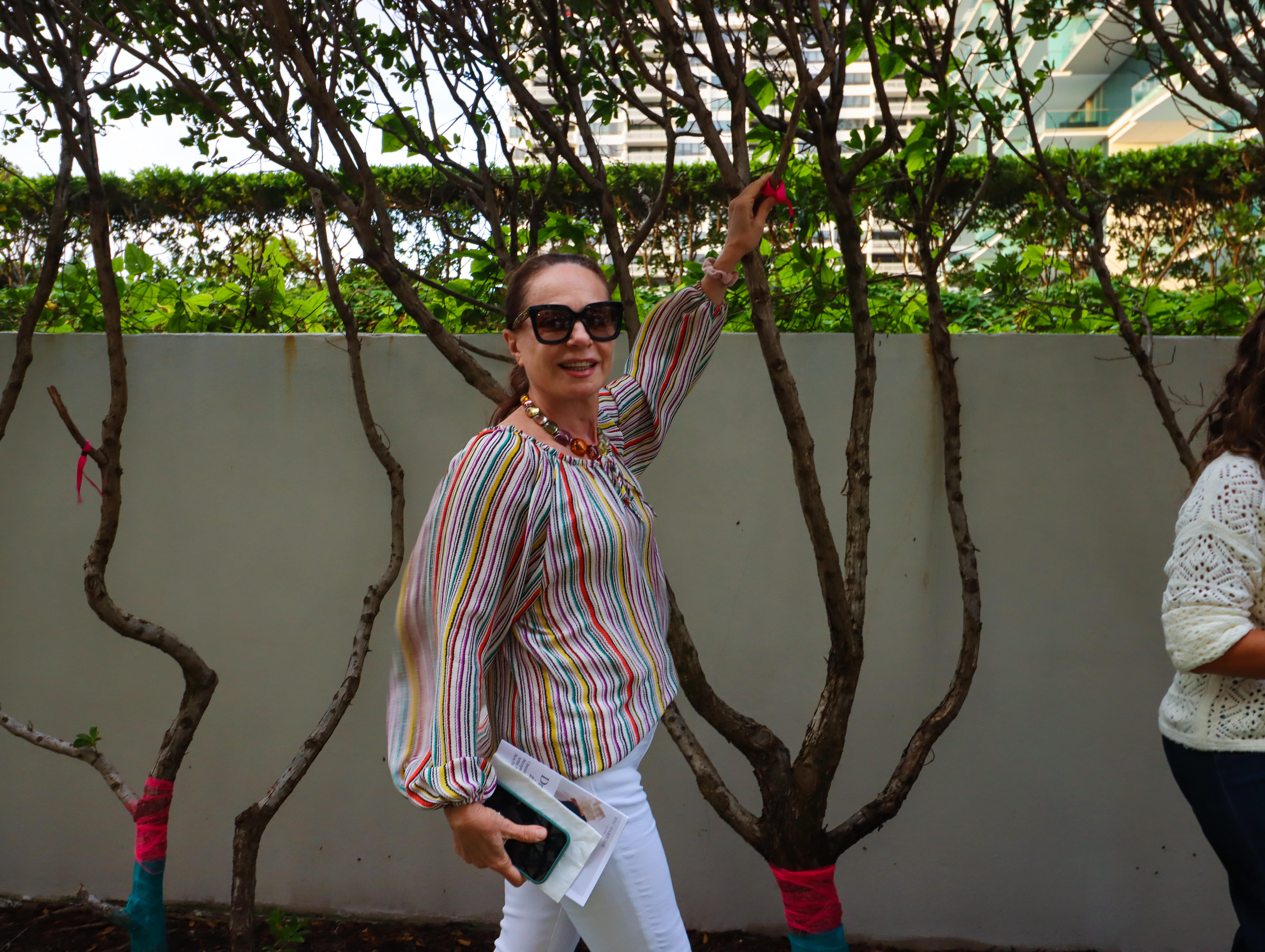 A woman walking and holding on to one of the wishing trees from the Dreaming in Color exhibit.