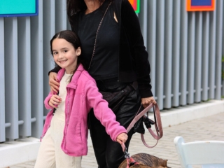 DIC7Compressed A mother holding onto her daughter, both grabbing the pink leash of a dog. Smiling for the camera in front of three paintings at the Dreaming In Color Exhibit.