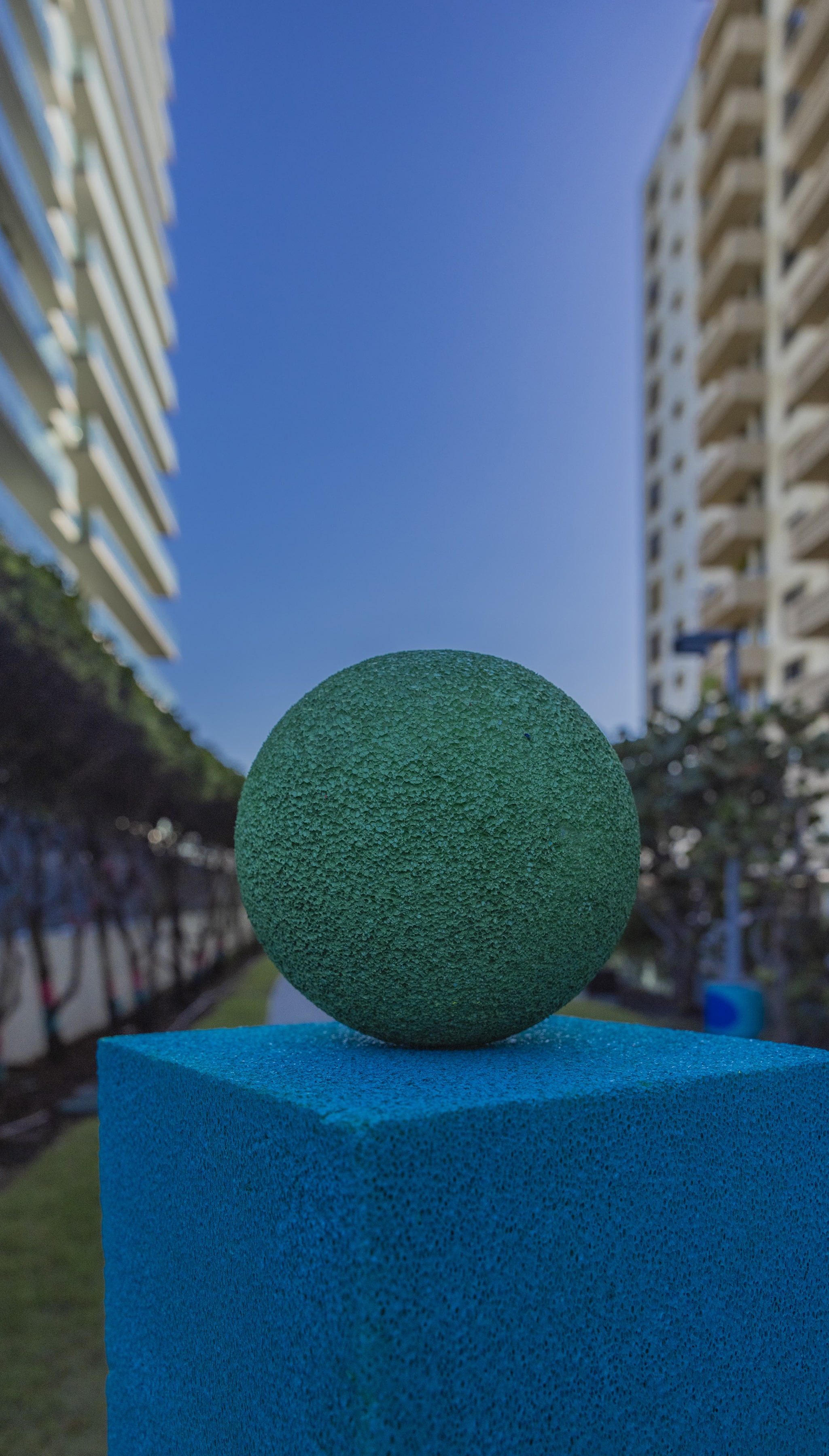 One of Artist Andreina Ron Pedrique&#039;s sculptures; a green ball over a blue square. The buildings and blue sky of Bal Harbour in the distance.