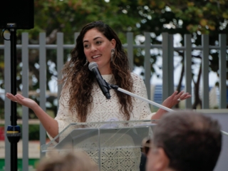DIC9Compressed A close-up of Artist Andreina Ron Pedrique speaking for a crowd into a microphone.