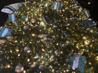 IMG_0537-min The holiday tree from a low angle, with lights and ornaments covering the tree. The Bal Harbour flag is slightly shown from behind the tree while the American flag is featured on the right.