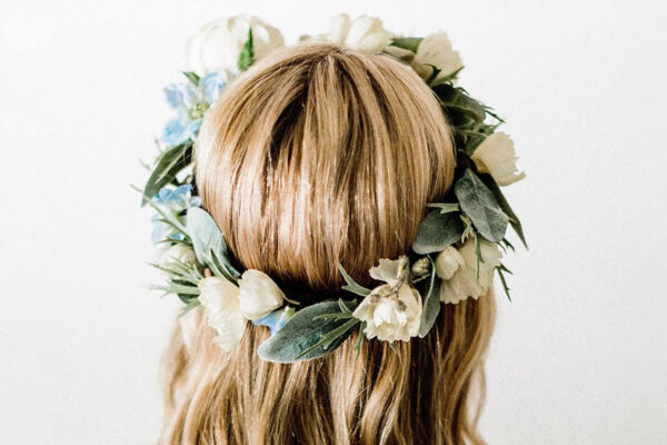 A beautiful floral crown made of fresh, vibrant flowers, resting on a girl's head. The crown features soft pastel blooms and greenery, adding a touch of elegance and nature to her look. The girl has long, flowing hair, and the soft sunlight highlights the delicate details of the crown, creating a serene, whimsical vibe.