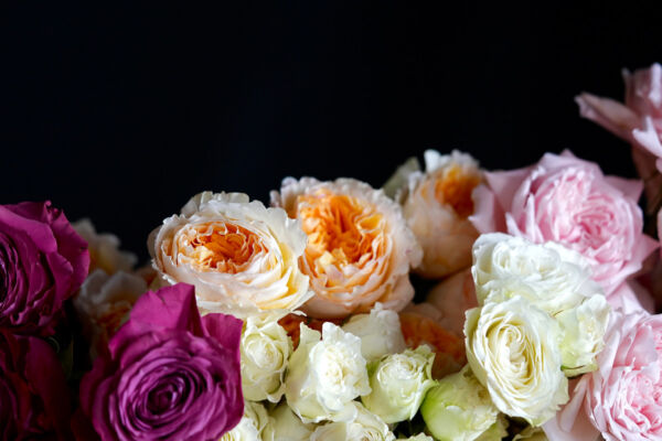 An arrangement of soft pastel-colored country roses in shades of pink, lavender, and cream, set in a rustic vase with delicate wildflowers and greenery. The overall scene evokes a charming, peaceful countryside atmosphere, perfect for a vintage-inspired floral display.