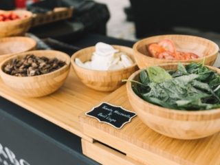 BalHarbourFilmFest-3-COMPRESSED An image of basil, tomatoes, mozzarella, and mushrooms all in separate wood bowls. There is a black tag that reads "Tomato Mozzarella & Basil Crepe" in front. All the bowls are placed on a wood table.