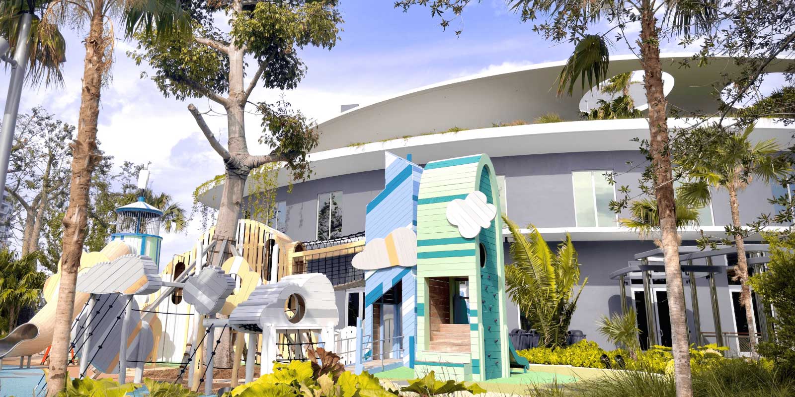 Exterior view of the Bal Harbour Waterfront Park, including the large playground, greenery, and the three-story community center.