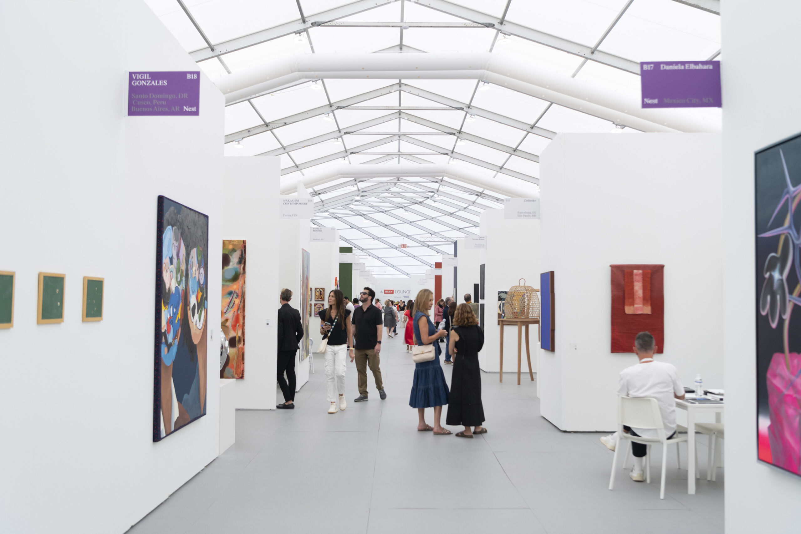 People walking around a room with various pieces of art work hanging on the walls