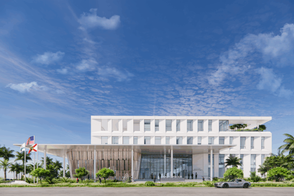 Modern four-story building with a sleek white facade, bordered by palm trees. U.S. and Florida flags wave in front. Clear blue sky above, creating an elegant atmosphere.