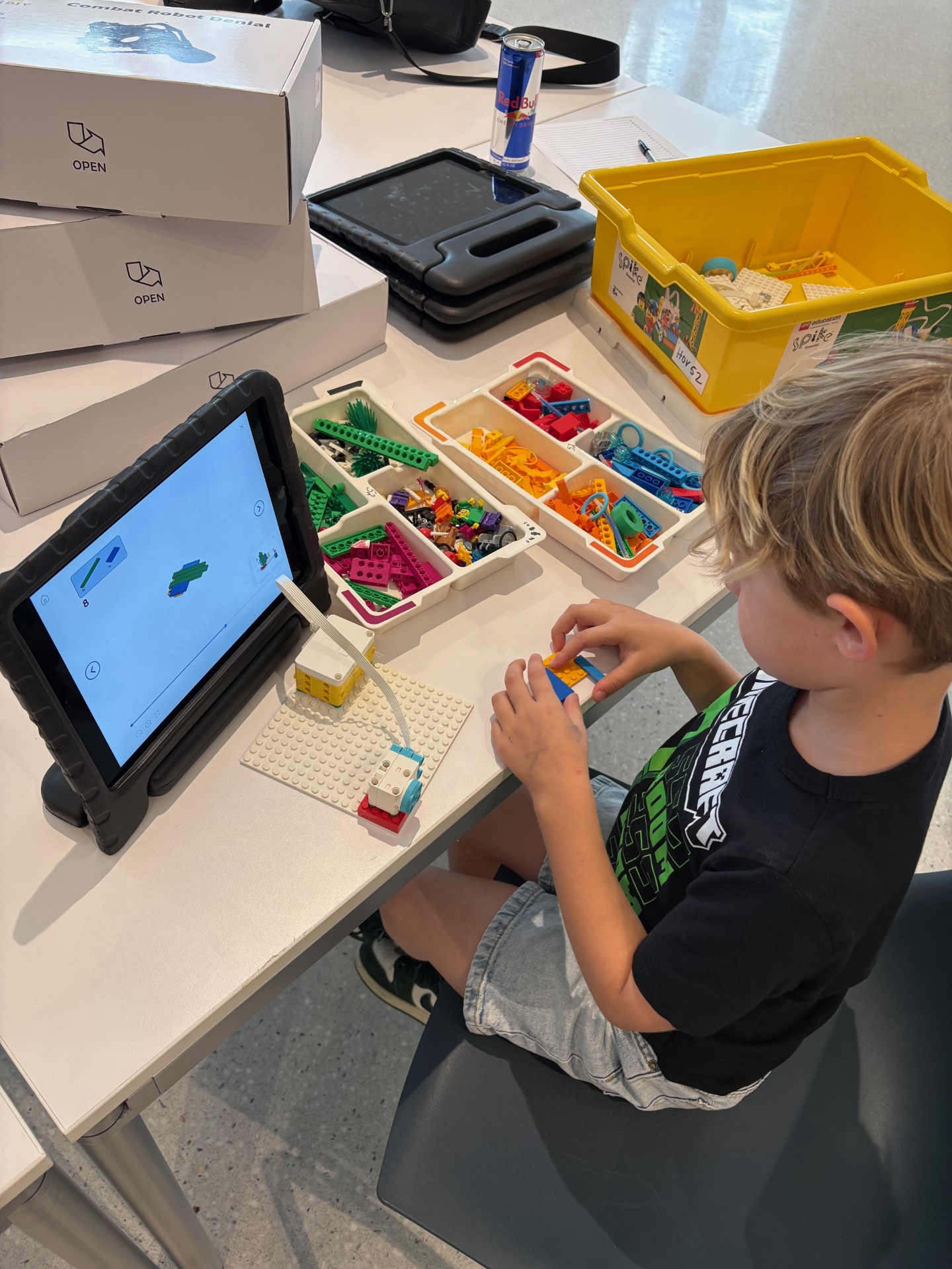 Child sitting at table with ipad and several boxes of legos, creating a project.