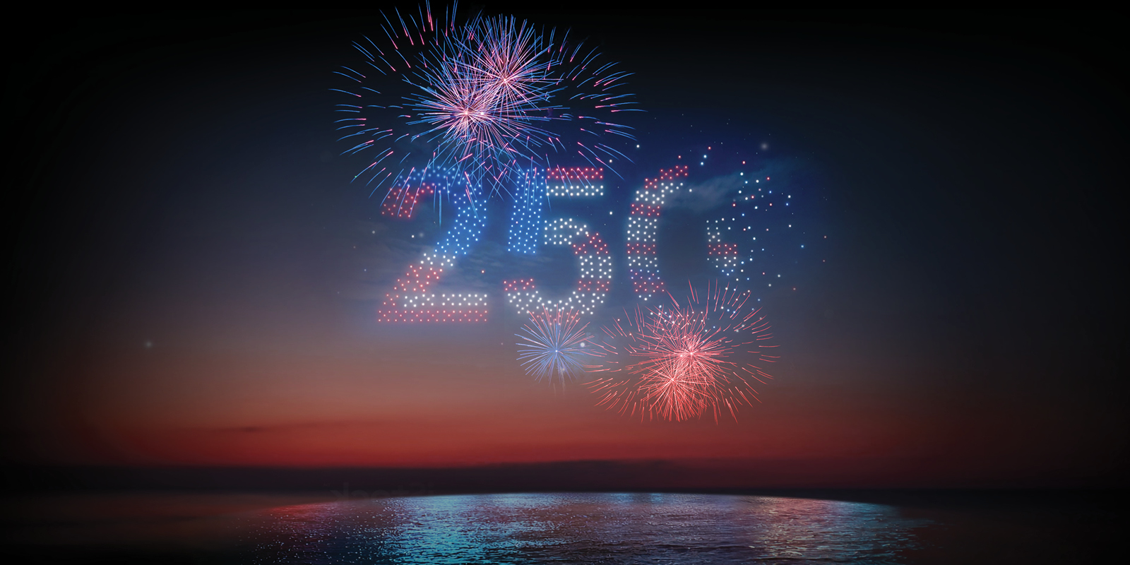 Fireworks form the number "250" in the night sky over a calm body of water at sunset.