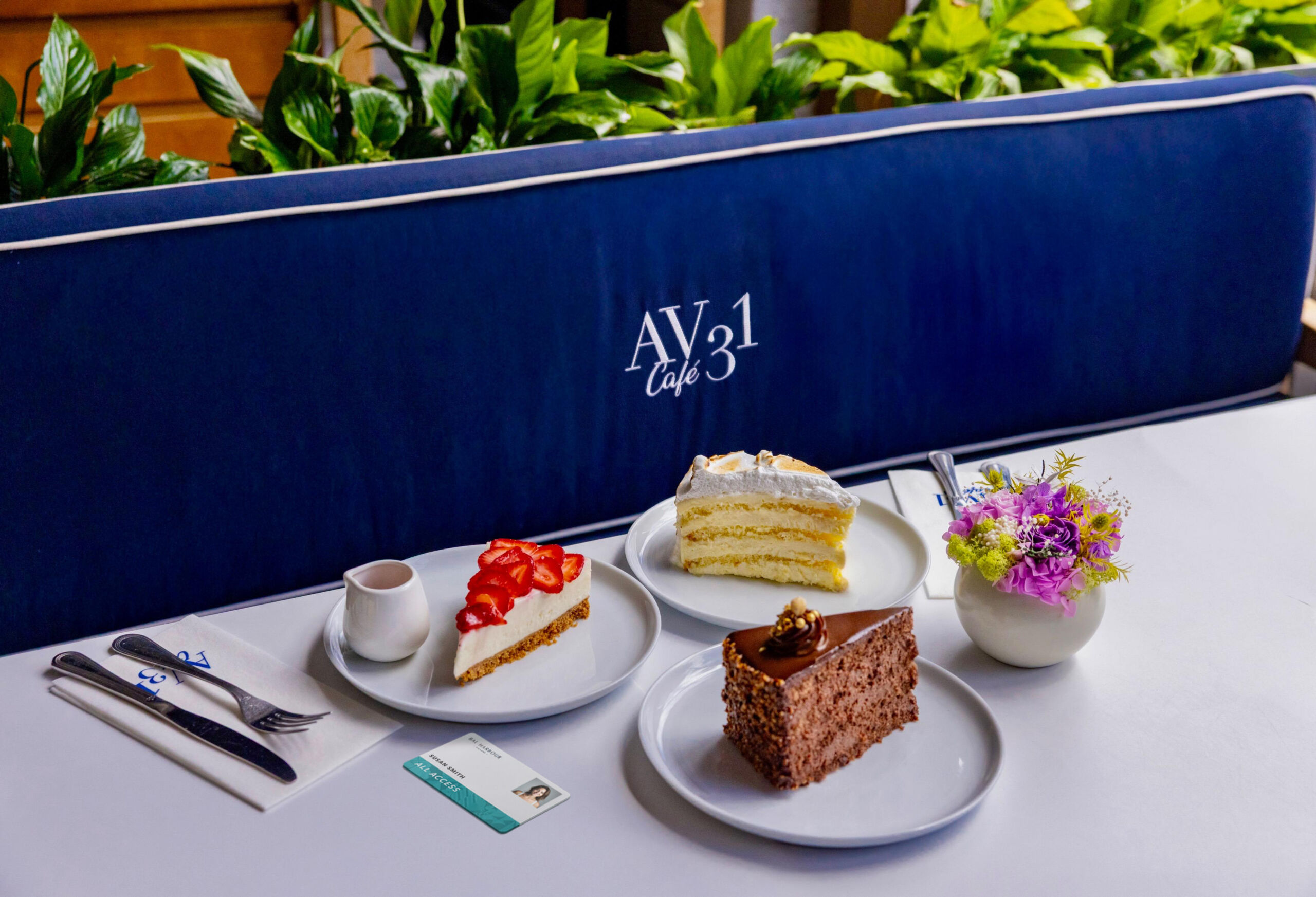Three plates with cake slices—a strawberry-topped, a layered white, and a chocolate one—are on a table with a small vase of flowers at Ave 31.